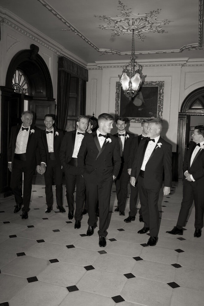 Groom and groomsmen stood in suits in a hall