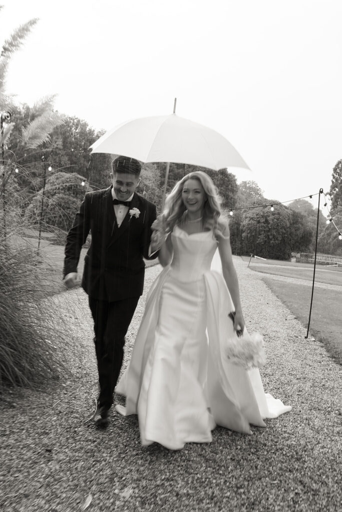 Bride and groom outside walking under umbrella